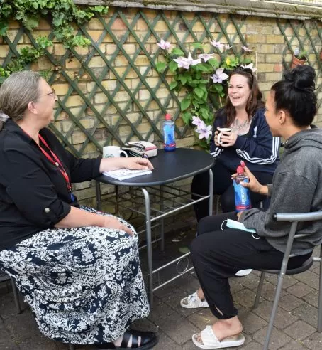 3 women seated at an outdoor table chatting and smiling.