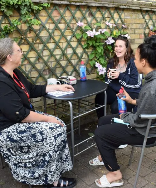 3 women seated at an outdoor table chatting and smiling.