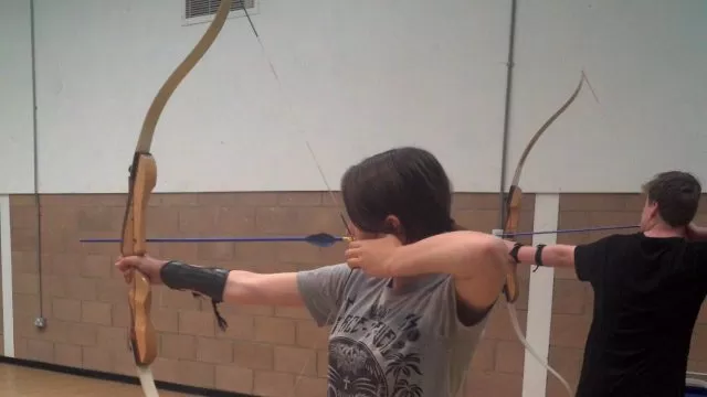 A young person pointing a bow and arrow to the left.