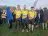 Three people standing side by side in running gear and Cambridgeshire Community Foundation branded yellow and blue tops. They're standing on grass with many people behind them.