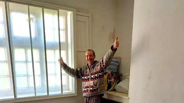 A person standing by the windows in a room, with his hands up in the air. His belongings are in