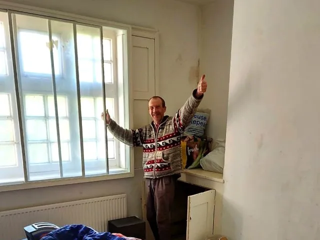 A person standing by the windows in a room, with his hands up in the air. His belongings are in