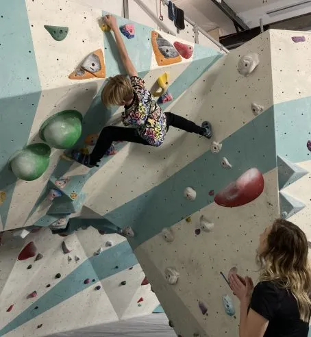 Child on a climbing frame and a person standing on the ground looking up at them and clapping.